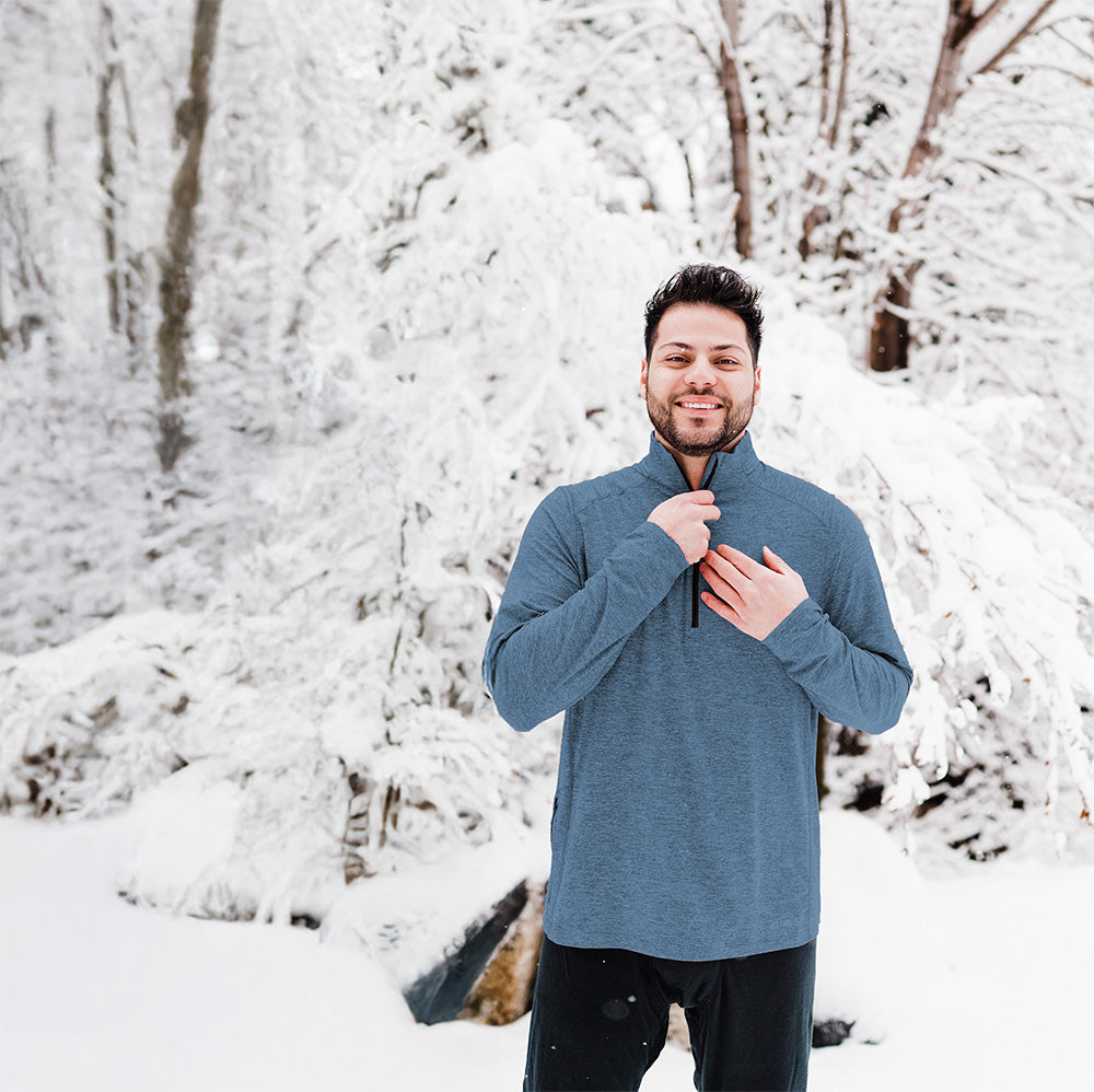 Man wearing a blue sweater standing in a snowy forest