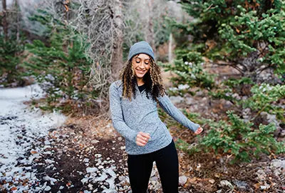 Woman wearing gray knit hat and light blue sweater enjoying a winter hike in a snowy forest