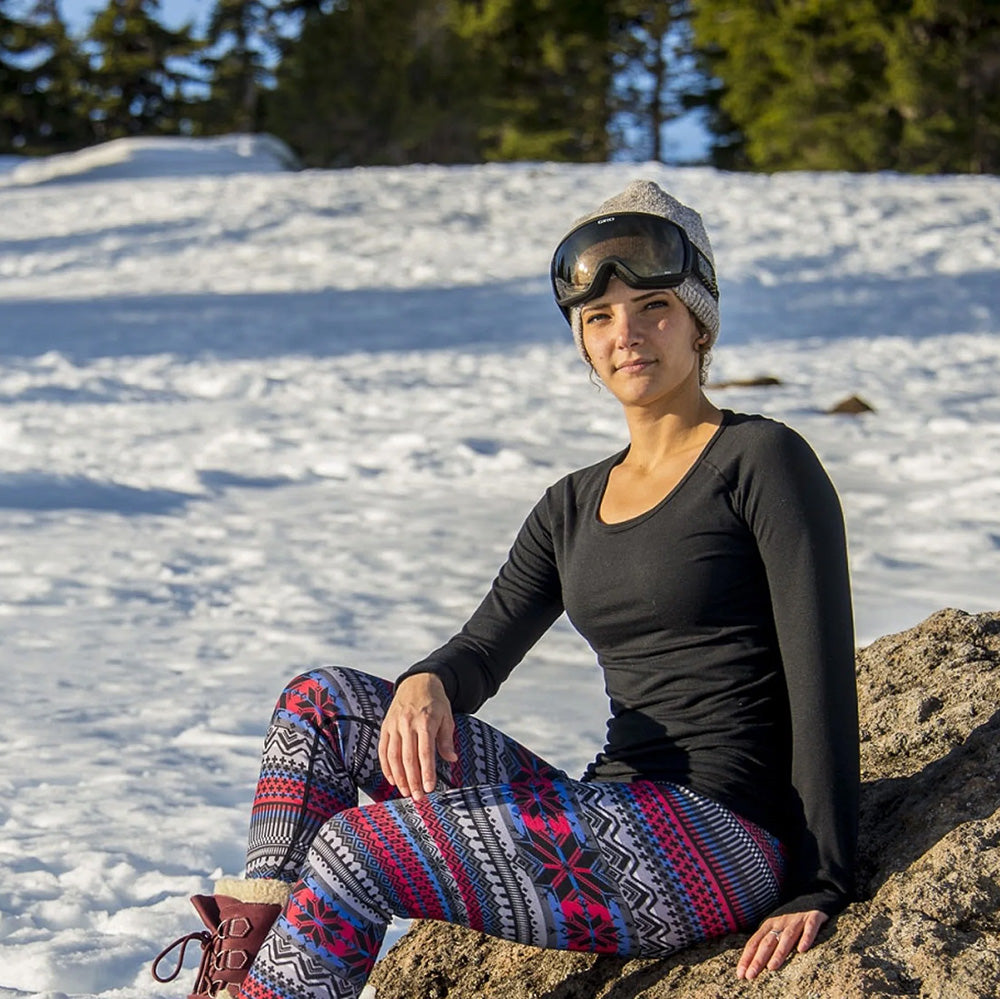 Person sitting on a rock in a snowy landscape wearing a black long-sleeve top and colorful patterned leggings.